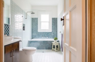 coastal bathrooms with blue scallop tile bathtub, shower and backsplash with dark wood vanity and white tile floors.