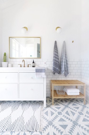 coastal bathroom with geometric floor tile, subway tile, white vanity, brass mirror and sconces, turkish towels, natural wood towel rack.