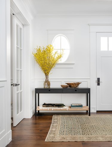 Mustard yellow foliage styled in an entryway on top of black console table with shelf for storage