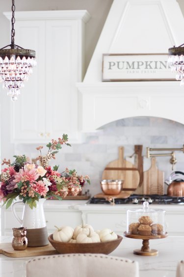 fall kitchen decor in white kitchen with flowers in a pitcher and pumpkins in a bowl