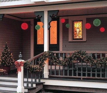 exterior Christmas decorations with Christmas garland and small Christmas tree lit with lights on front porch with red and green globe lights.
