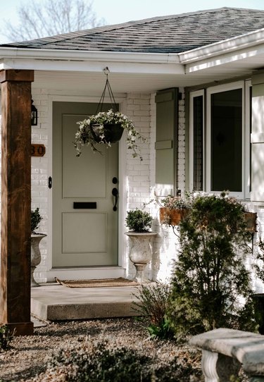 Soft green exterior house paint on front door and shutters with painted white brick exterior