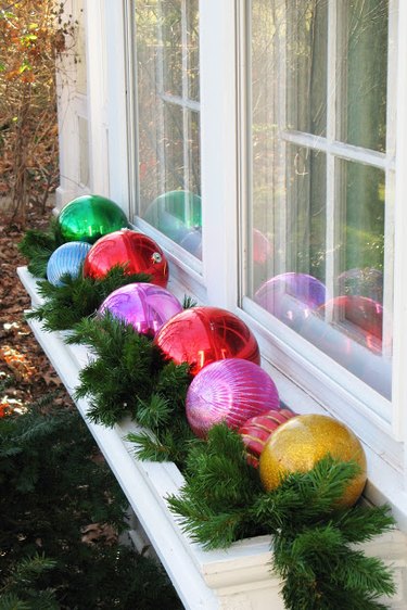 exterior Christmas decorations with Multi-colored Christmas ball ornaments and artificial greenery inside window box.
