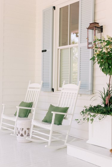 Light blue louvered exterior shutter style on white home alongside white rocking chairs