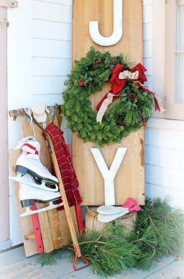 exterior Christmas decorations with DIY Joy sign with wreath, ice skates, sled, greenery.