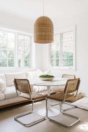 white dining room with cane dining chairs and bell-shaped pendant