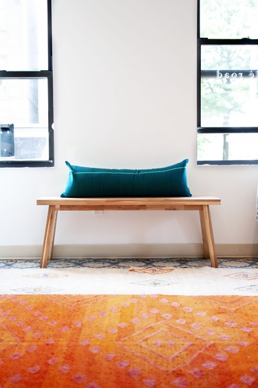 long accent pillow on wooden bench in front of windows