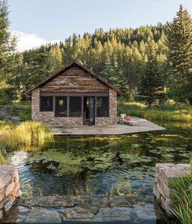 stone and wood modern cabin surrounded by water and trees