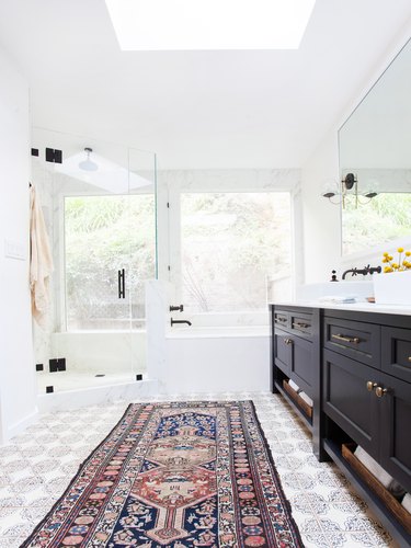 white bathroom with black vanity cabinet and area rug on patterned tile