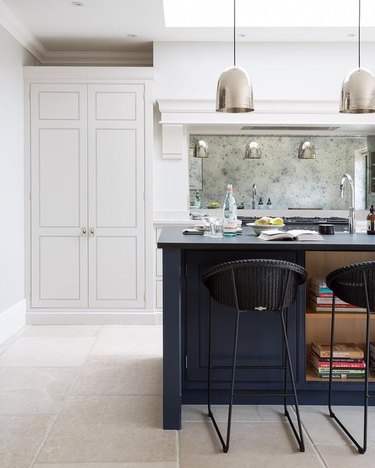 limestone kitchen flooring with blue island and white cabinets paired with mirror backsplash