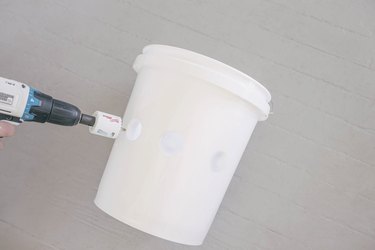 Drilling three holes in front of plastic bucket with hole saw