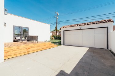 A white garage with a Spanish-style roof, a concrete driveway that is next to a wooden deck