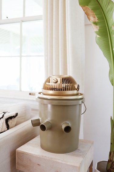 Green and gold portable bucket air conditioner on an end table next to a couch