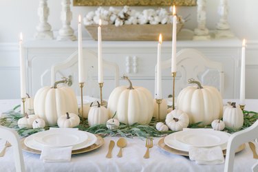 DIY fall decor idea with white pumpkin centerpiece on white tablecloth table with taper candles