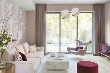 pink room ideas with Pink couch, pink lounge chair, red pouf, marble coffee table, pink walls, pink wallpaper, pink curtains, white pendants lights.