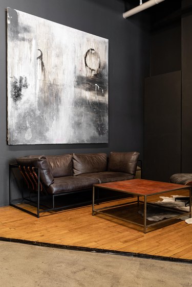 Living room with dark gray walls, an abstract painting, brown leather sofa, and square coffee table.