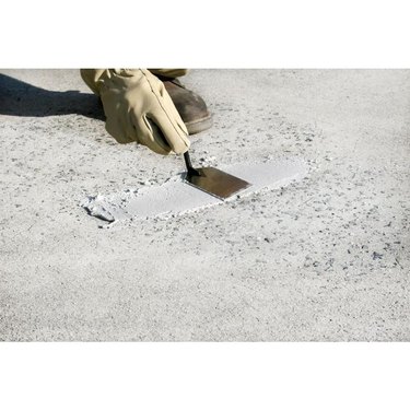 A person patching a concrete driveway with a trowel.