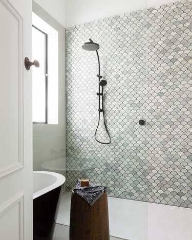 Handheld showerhead in open shower with green mosaic wall tile