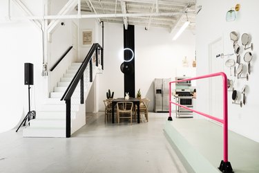 open room with neon pink handrail, dining table, concrete floor, staircase