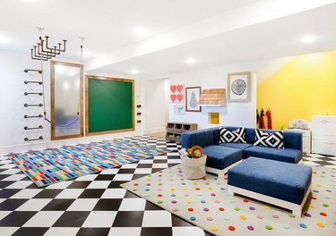basement ideas with Black and white checker floors, multi colored area rug, navy blue sectional, yellow accent wall, chalkboard, climbing wall and ceiling.