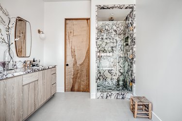 A bathroom with a marble shower, a wood vanity, and a wood door