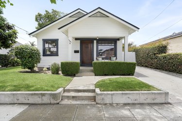 white craftsman home with green grass and some evergreen shrubs