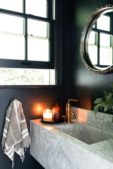 Marble sink in bathroom with dark blue painted walls and brass faucet