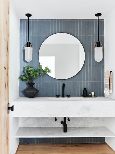 undermount bathroom sink with blue tile accent wall and pair of pendants framing round mirror