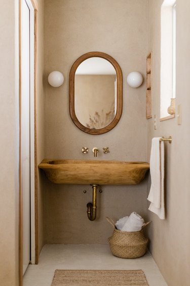 Bathroom with wood sink with natural elements, wood framed mirror and white sconces