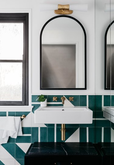 modern bathroom lighting with arched mirror above wall-mounted sink with green wall tile