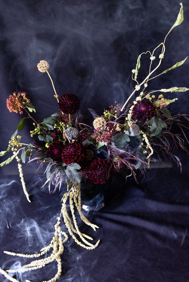 ornate flower arrangement with dark-colored flowers and smoke in background