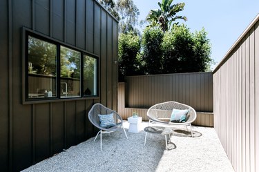 a side yard of a modern home with a pea gravel patio, white mid-century modern patio furniture