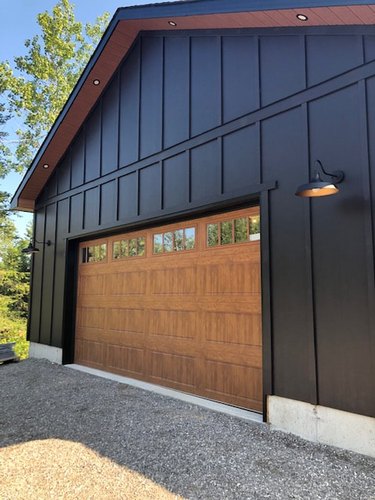 black home exterior with wood garage door and sconces