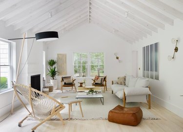 coastal living room with wicker Acapulco chair, leather pouf, white couch, white arch ceilings, light wood floor.