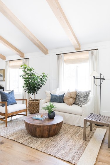 Rustic living room with wood coffee table, jute rug, couch, pillows, chair, large plant, wood beam ceiling,