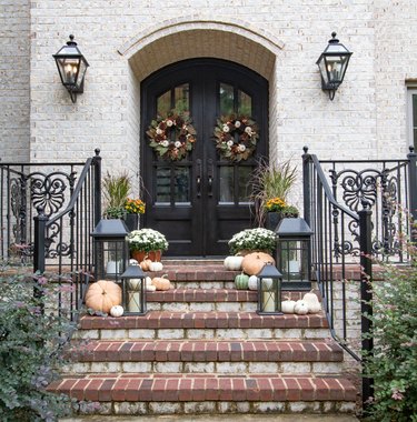 fall porch decor with white exterior with black door and pumpkins on steps