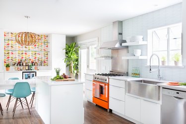 Bright kitchen with white cabinets, an orange stove, stainless steel sink and bright feature wall