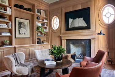 Home office library with wood walls and leather armchairs by Amber Interiors