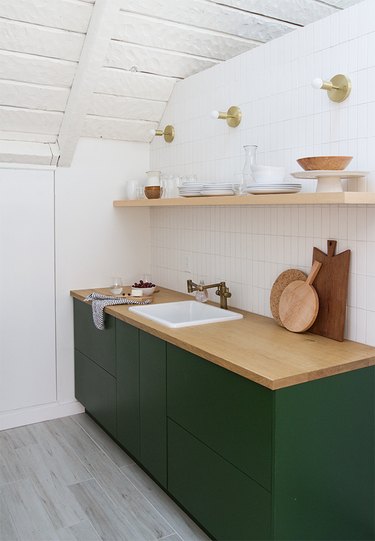 Simple white subway tile backsplash in minimalist kitchen with green cabinets and wood countertop