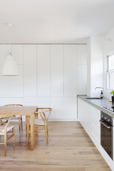 White floor-to-ceiling cabinets in minimalist kitchen with wood dining table and chairs