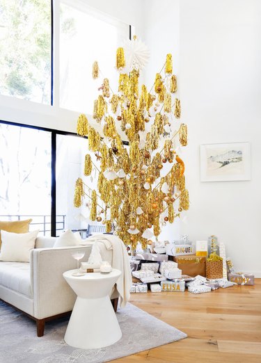 Christmas Tree Themes with Gold pompom Christmas tree, white couch, white side table, wood flooring.
