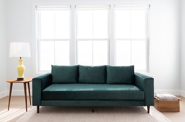 green couch near table with lamp and windows