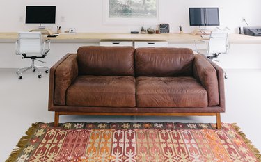 Home Office for Two Leather couch, area rug, side by side work stations with computer screens and white desk chairs.