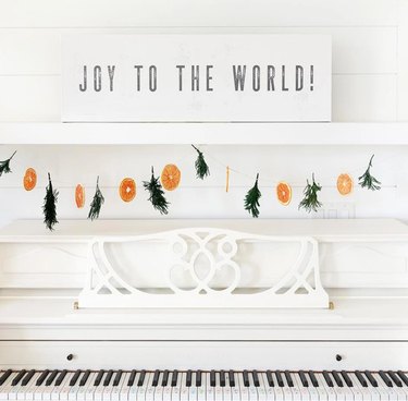 Joy to the World farmhouse Christmas decor with canvas sign on white piano with dried orange and juniper garland