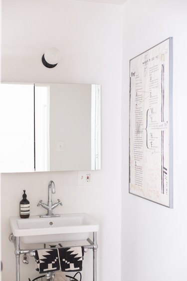 white ceramic console sink, mirrored medicine cabinet, round white light fixture, black patterned hand towels, white poster with text