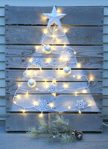 Pallet Christmas tree with painted-on shape, twinkle lights, and attached ornaments