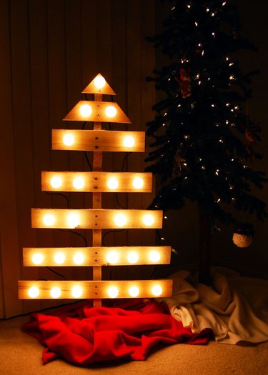 Pallet Christmas tree with attached lights in modern shape next to Christmas decorations