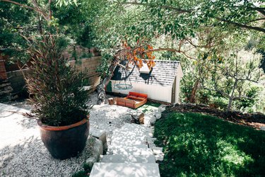 A sloped yard with concrete steps, green grass, potted plants and lots of shade from trees