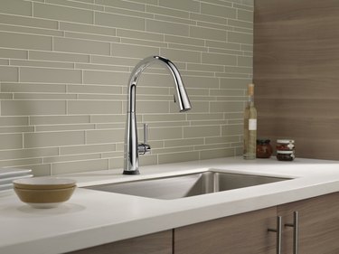A stainless steel Delta kitchen faucet in a kitchen with a white counter and a green tile backsplash