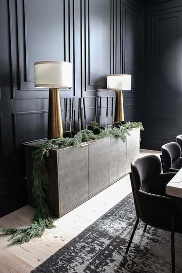 Black dining room with black accent wall, tapered candles, brass lamps, and ornaments in greenery